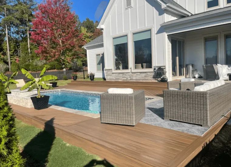 Brown composite deck wrapping an in-ground pool at a modern farmhouse with wicker lounge seating