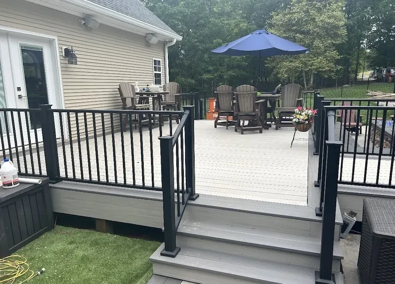 Gray composite deck with black aluminum railing, steps to the lawn and Adirondack chair seating