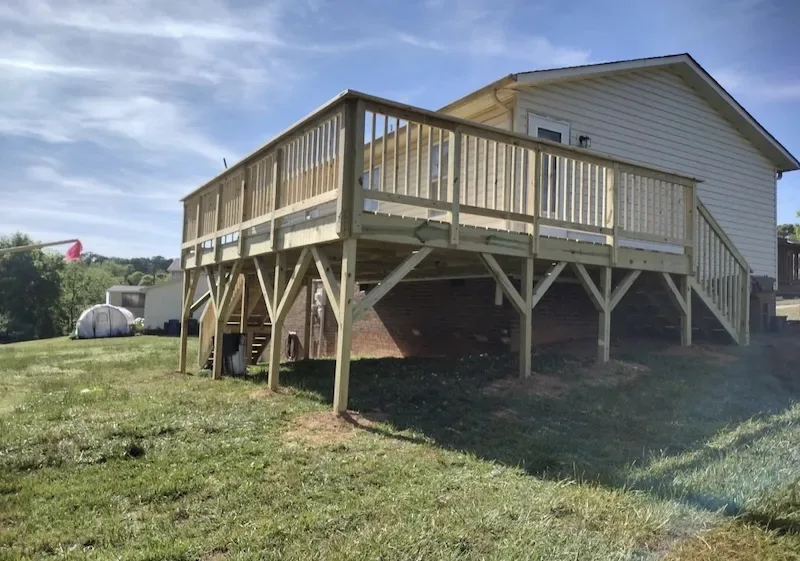 Large elevated pressure-treated wood deck on tall support posts with a long staircase